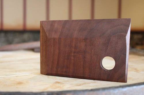 Tapered wooden bench scraper standing upright. Has hanging hole