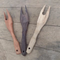 Two pronged wooden charcuterie forks displayed on wooden surface.