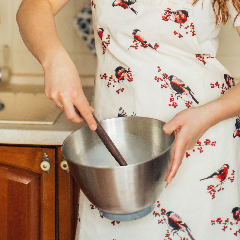Person holding a metal mixing bowl with a wooden spoon, wearing a floral apron.